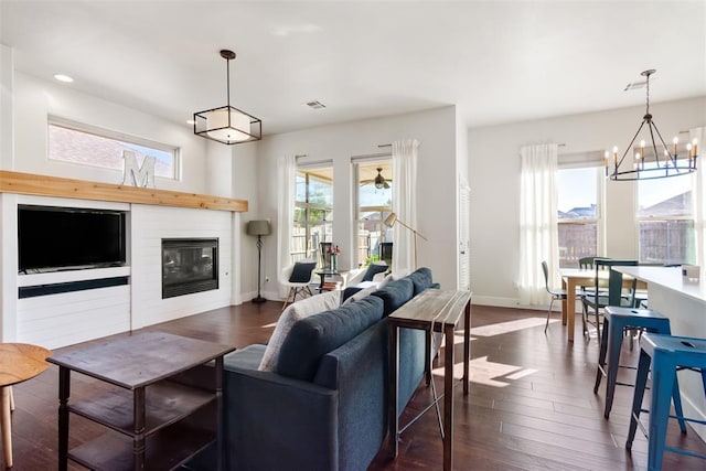 living room featuring a fireplace, an inviting chandelier, plenty of natural light, and dark wood-type flooring