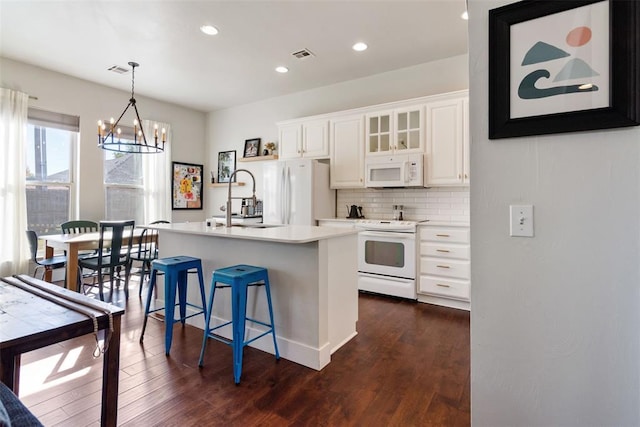 kitchen with white cabinetry, white appliances, an island with sink, and a chandelier