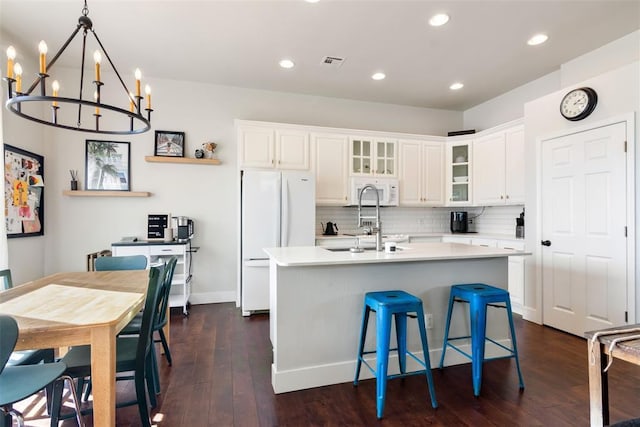 kitchen with white appliances, white cabinetry, a notable chandelier, and an island with sink