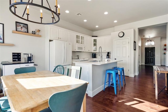 kitchen featuring a center island with sink, decorative light fixtures, white cabinets, and white appliances