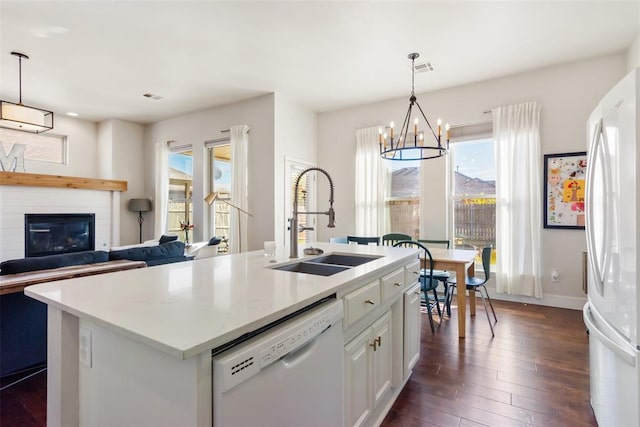 kitchen with sink, an island with sink, hanging light fixtures, and white appliances