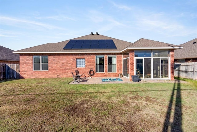 back of property featuring a patio area, a sunroom, a yard, and solar panels