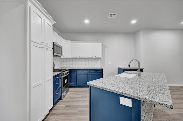 kitchen with sink, stainless steel appliances, blue cabinets, an island with sink, and white cabinets