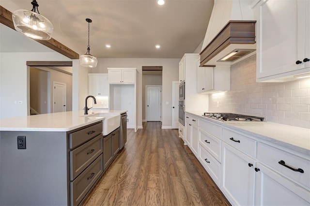 kitchen featuring stainless steel appliances, sink, a center island with sink, white cabinetry, and hanging light fixtures