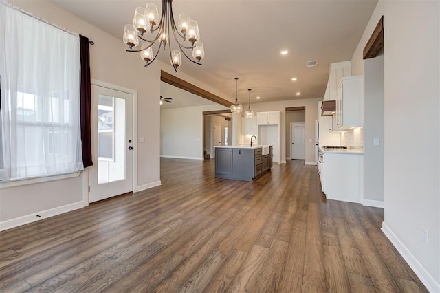 unfurnished living room with ceiling fan with notable chandelier, sink, and dark wood-type flooring