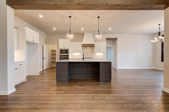 kitchen with built in microwave, decorative light fixtures, a center island with sink, white cabinets, and oven