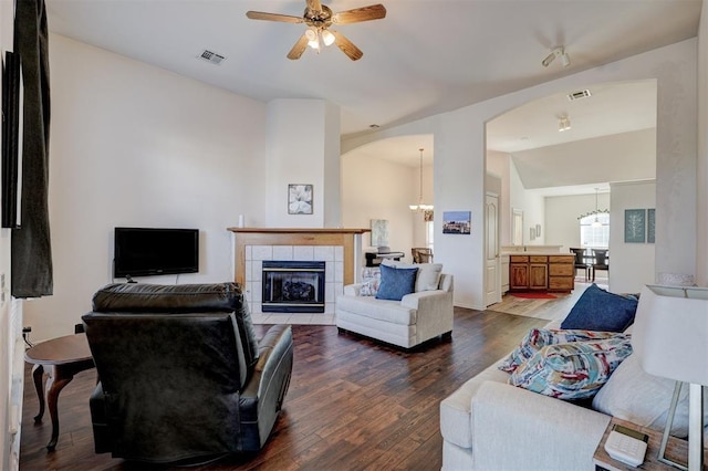 living room with a tile fireplace, dark hardwood / wood-style flooring, ceiling fan with notable chandelier, and vaulted ceiling