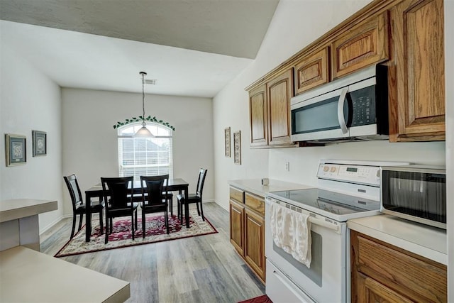 kitchen featuring decorative light fixtures, electric stove, light hardwood / wood-style flooring, and vaulted ceiling