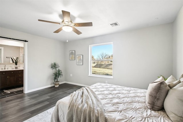 bedroom with ensuite bathroom, a barn door, dark wood-style flooring, visible vents, and baseboards