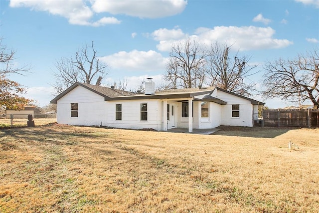 rear view of property featuring a yard, a chimney, and fence