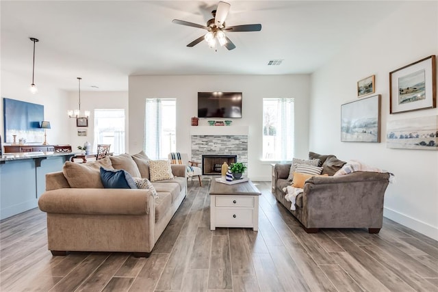 living area with ceiling fan with notable chandelier, a fireplace, wood finished floors, visible vents, and baseboards