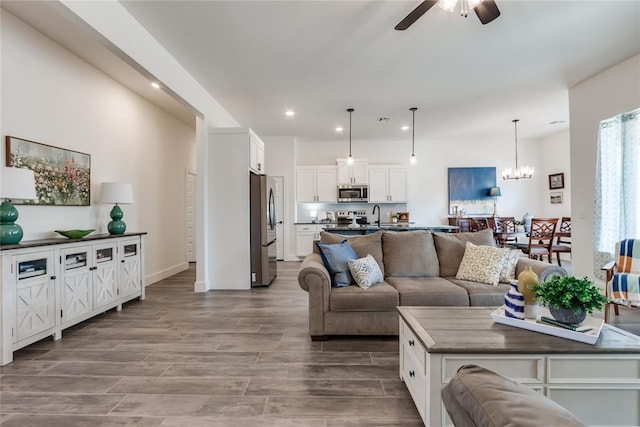 living area with wood finish floors, recessed lighting, and ceiling fan with notable chandelier