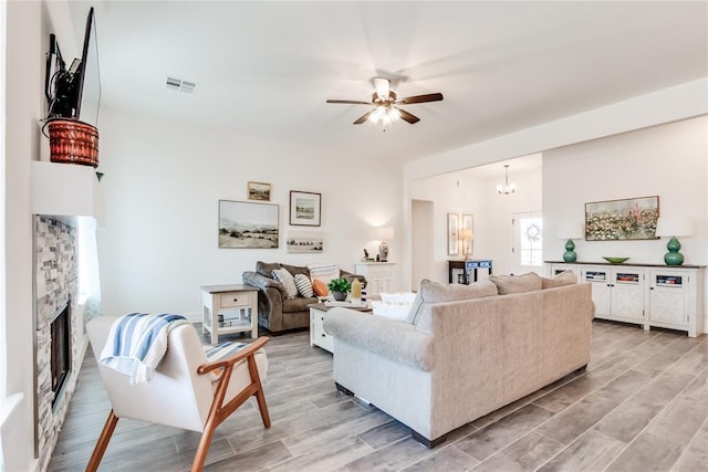 living room featuring a ceiling fan, a fireplace, visible vents, and wood tiled floor