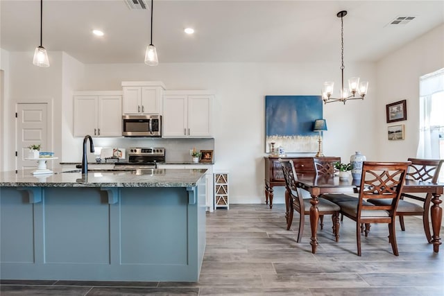 kitchen with stainless steel appliances, wood finished floors, visible vents, decorative backsplash, and dark stone counters