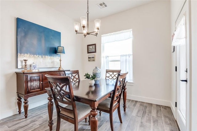 dining area with baseboards, light wood finished floors, visible vents, and an inviting chandelier