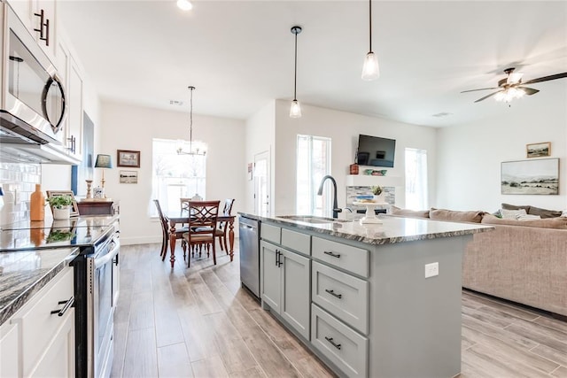 kitchen with light stone counters, open floor plan, stainless steel appliances, wood finish floors, and a sink