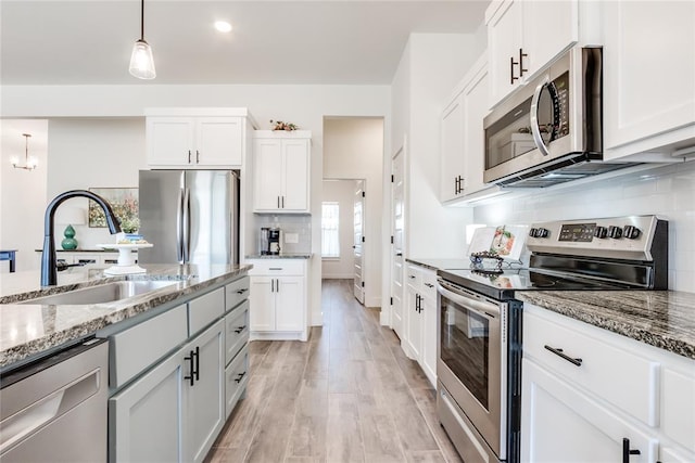 kitchen featuring backsplash, appliances with stainless steel finishes, a sink, light stone countertops, and light wood-type flooring