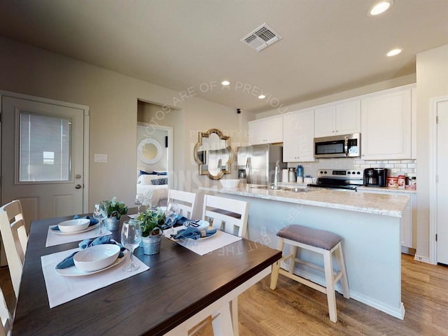 kitchen with decorative backsplash, light stone countertops, stainless steel appliances, light hardwood / wood-style floors, and white cabinetry