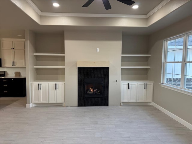 unfurnished living room with a fireplace, ornamental molding, built in shelves, a raised ceiling, and light wood-type flooring