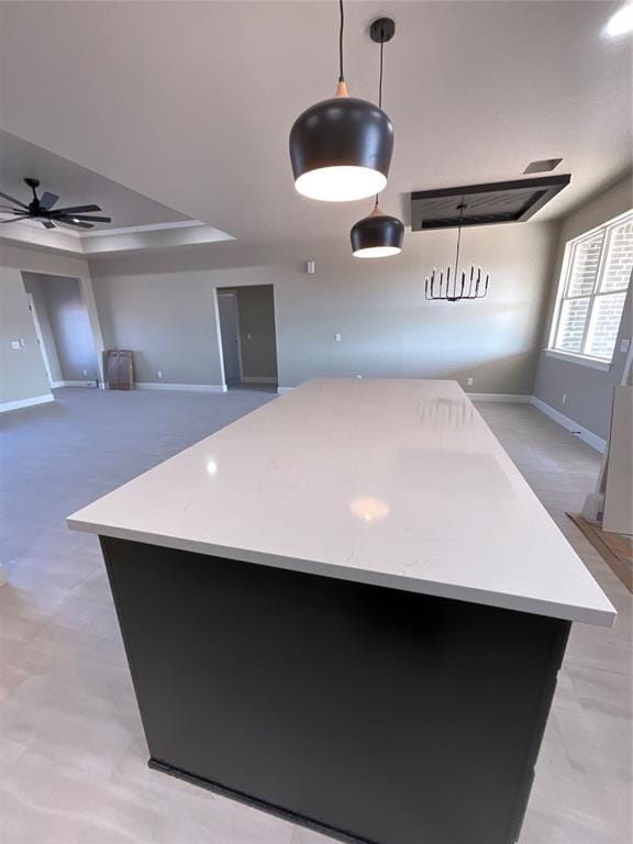 kitchen featuring ceiling fan, decorative light fixtures, a center island, and a raised ceiling