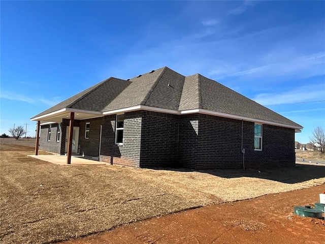 view of property exterior with brick siding, a shingled roof, and a patio