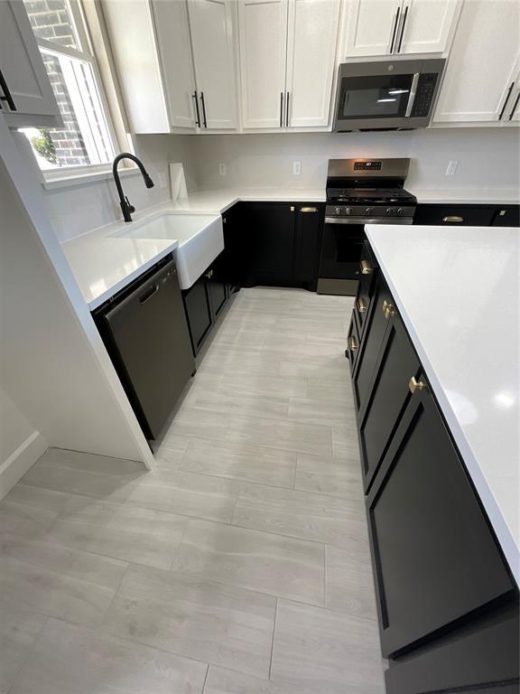 kitchen with light countertops, appliances with stainless steel finishes, dark cabinetry, white cabinets, and a sink