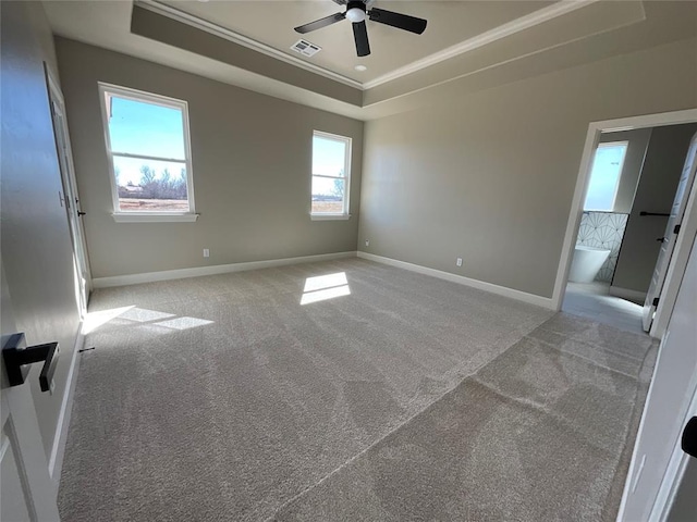 carpeted empty room featuring visible vents, a raised ceiling, baseboards, and ornamental molding