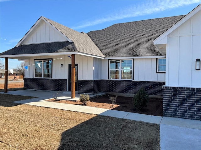 modern farmhouse with board and batten siding, brick siding, and a shingled roof