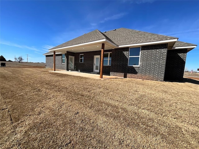 back of property with brick siding, a shingled roof, and a patio area