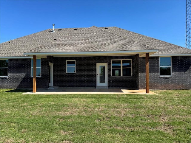 back of house featuring brick siding, a shingled roof, a patio area, and a lawn
