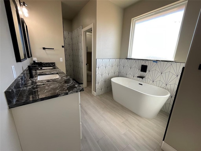 bathroom with double vanity, tile walls, a sink, toilet, and a soaking tub