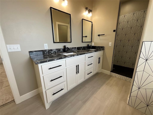 bathroom featuring double vanity, a sink, walk in shower, and wood finished floors