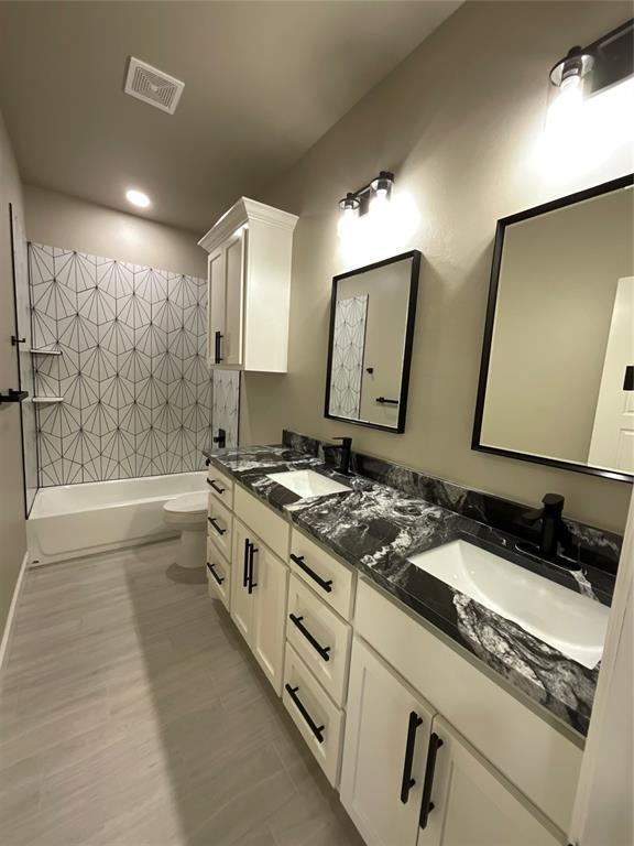 full bath with a sink, toilet, double vanity, and visible vents
