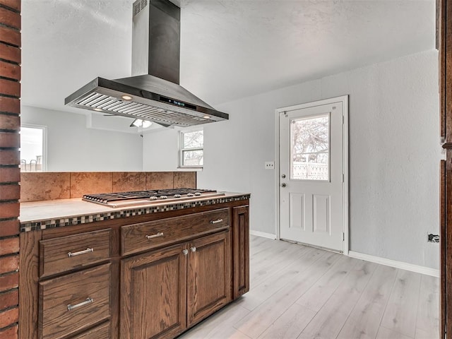 kitchen featuring stainless steel gas stovetop, wall chimney range hood, and light hardwood / wood-style flooring