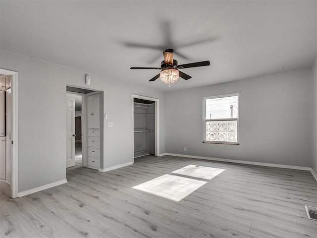 unfurnished bedroom with ceiling fan, a closet, a walk in closet, and light hardwood / wood-style flooring