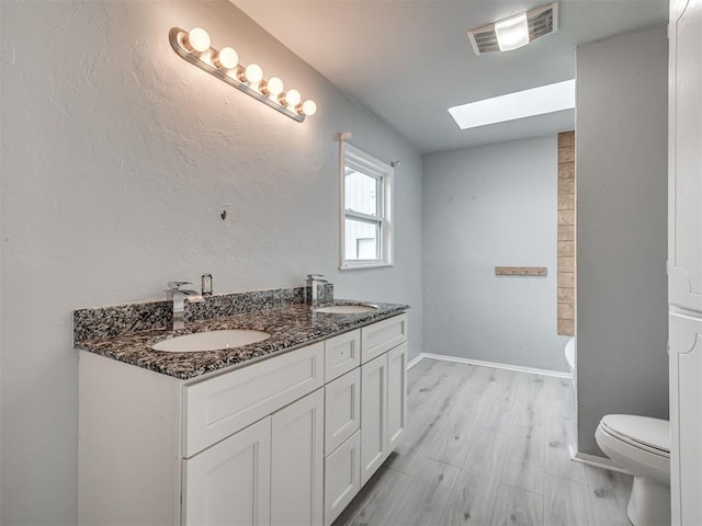 bathroom featuring hardwood / wood-style floors, vanity, toilet, and a skylight