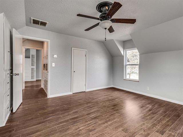 additional living space with a textured ceiling, ceiling fan, lofted ceiling, and dark wood-type flooring