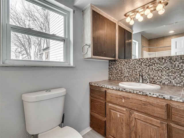 bathroom featuring toilet, vanity, baseboards, decorative backsplash, and walk in shower