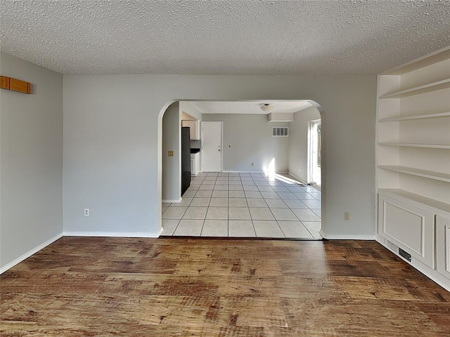 spare room featuring light wood-type flooring, built in shelves, and a textured ceiling