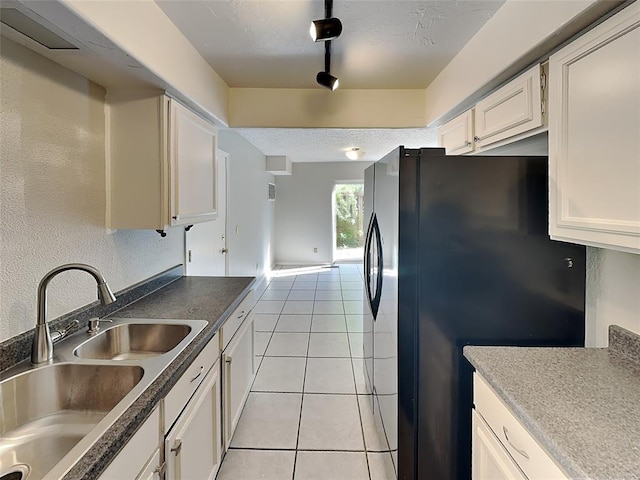 kitchen featuring white cabinetry, sink, track lighting, black refrigerator, and light tile patterned floors