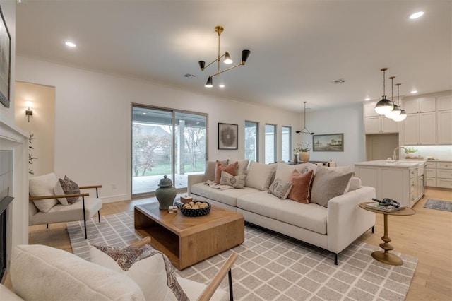 living room with sink, light hardwood / wood-style flooring, ornamental molding, and a notable chandelier