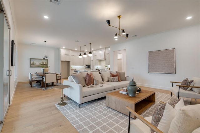 living room with a chandelier, light wood-type flooring, and ornamental molding