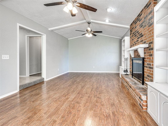 unfurnished living room featuring built in shelves, a brick fireplace, vaulted ceiling with beams, hardwood / wood-style floors, and a textured ceiling