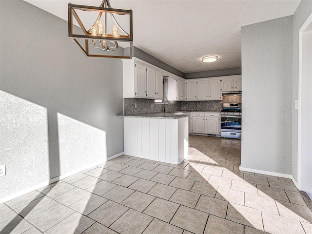 kitchen with sink, stainless steel range, tasteful backsplash, a notable chandelier, and white cabinetry