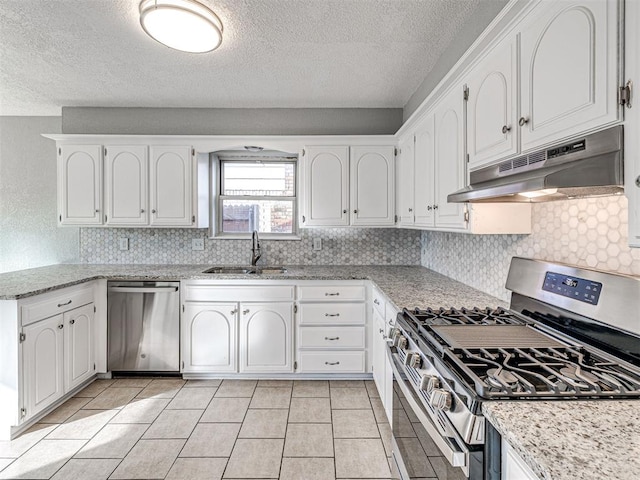 kitchen featuring appliances with stainless steel finishes, light stone counters, sink, light tile patterned floors, and white cabinetry