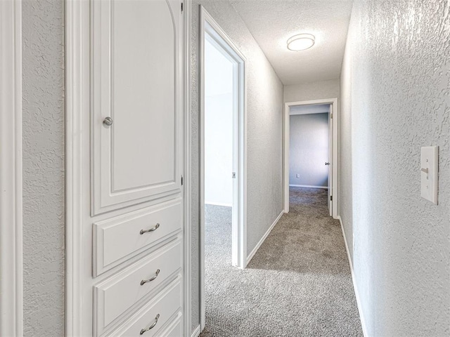 hallway with a textured ceiling and light carpet