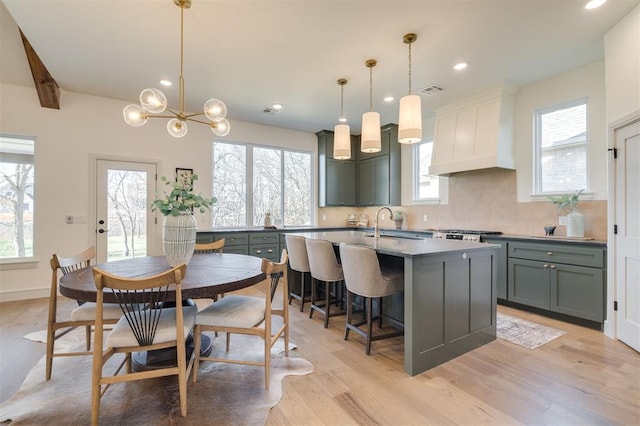 kitchen featuring backsplash, premium range hood, pendant lighting, a center island with sink, and a chandelier