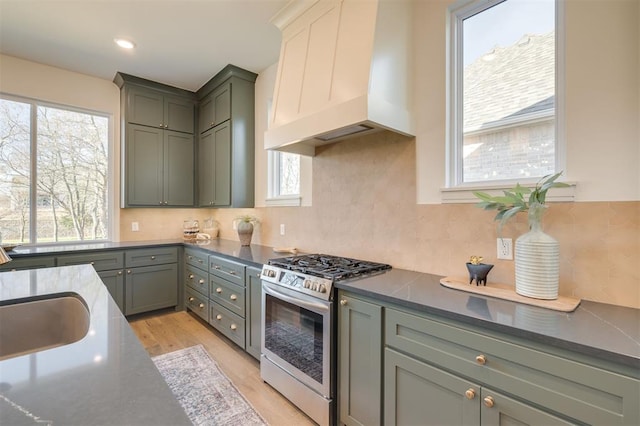 kitchen featuring sink, stainless steel gas range oven, light hardwood / wood-style flooring, decorative backsplash, and custom exhaust hood