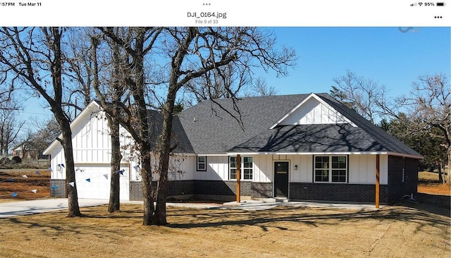 modern farmhouse style home featuring driveway, board and batten siding, a front yard, a shingled roof, and brick siding