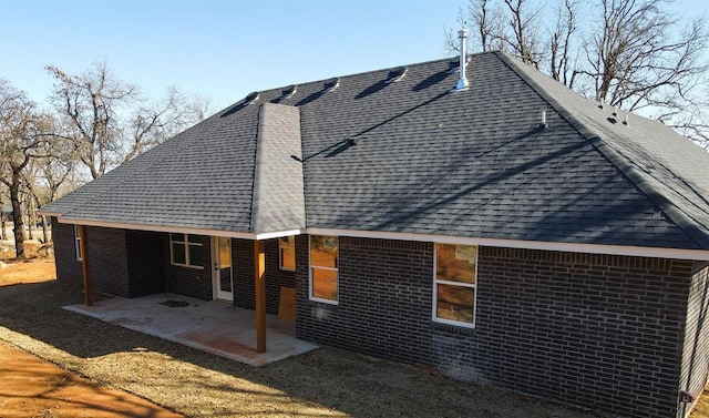 exterior space featuring a patio, brick siding, and roof with shingles